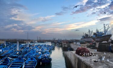 A serene scene of blue fishing boats docked at sunset in a Moroccan harbor.