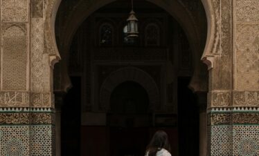 A woman walks by a beautifully decorated archway of a Moroccan mosque in Fes, showcasing traditional Islamic architecture.