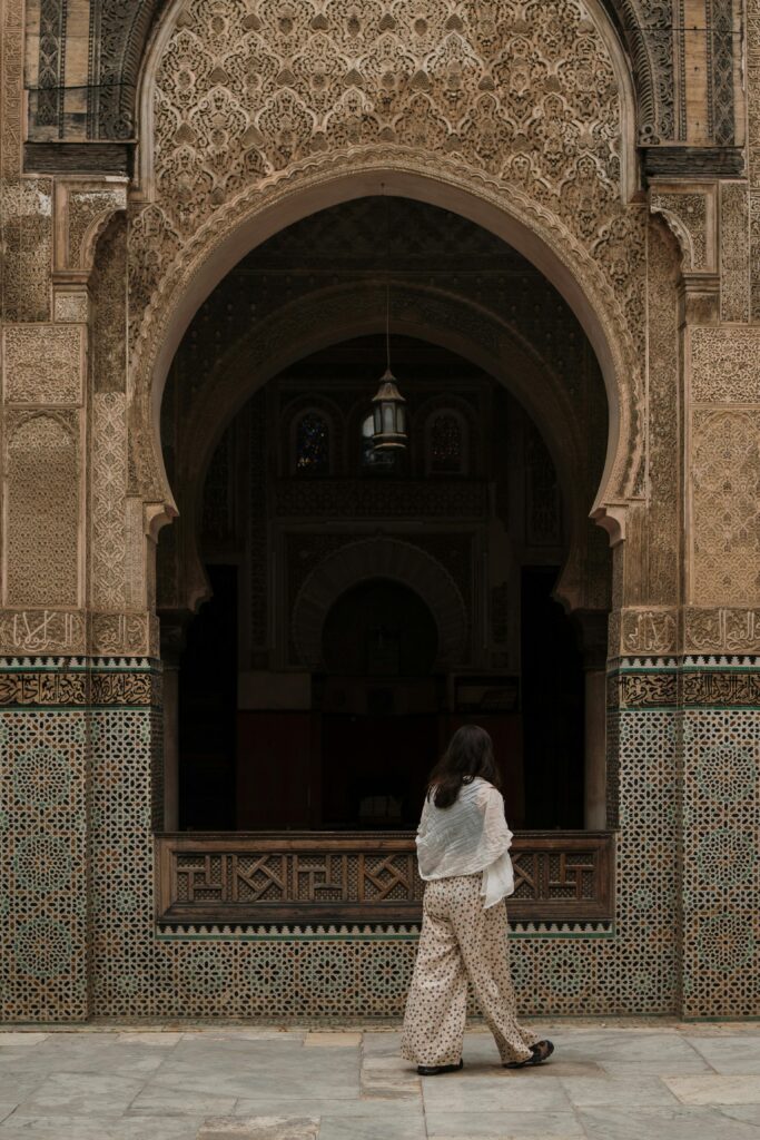A woman walks by a beautifully decorated archway of a Moroccan mosque in Fes, showcasing traditional Islamic architecture.