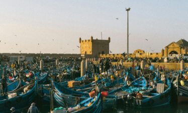 Colorful fishing boats moored in the bustling port of Essaouira, Morocco, with historic fortifications in view.