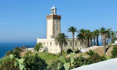 A scenic view of Cape Spartel Lighthouse surrounded by lush palm trees on a sunny day in Morocco.