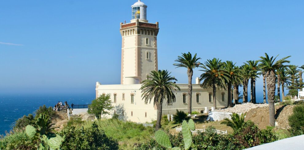 A scenic view of Cape Spartel Lighthouse surrounded by lush palm trees on a sunny day in Morocco.