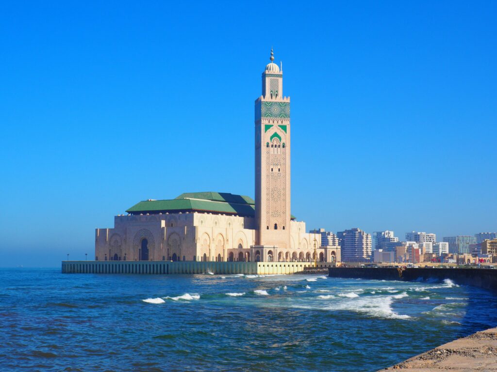 Hassan II Mosque in Casablanca against a vibrant blue sky and ocean waves.