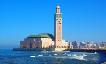 Hassan II Mosque in Casablanca against a vibrant blue sky and ocean waves.