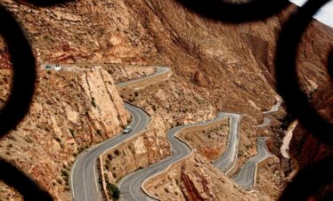 Scenic view of a winding road through the Atlas Mountains framed by ornate ironwork.