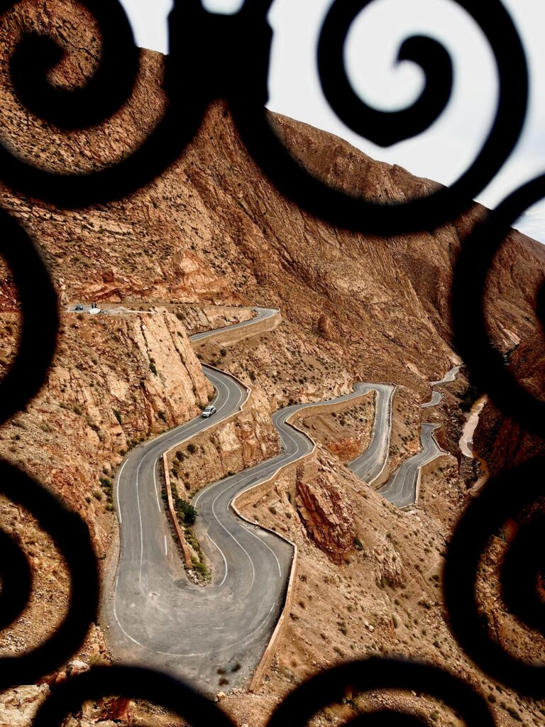 Scenic view of a winding road through the Atlas Mountains framed by ornate ironwork.