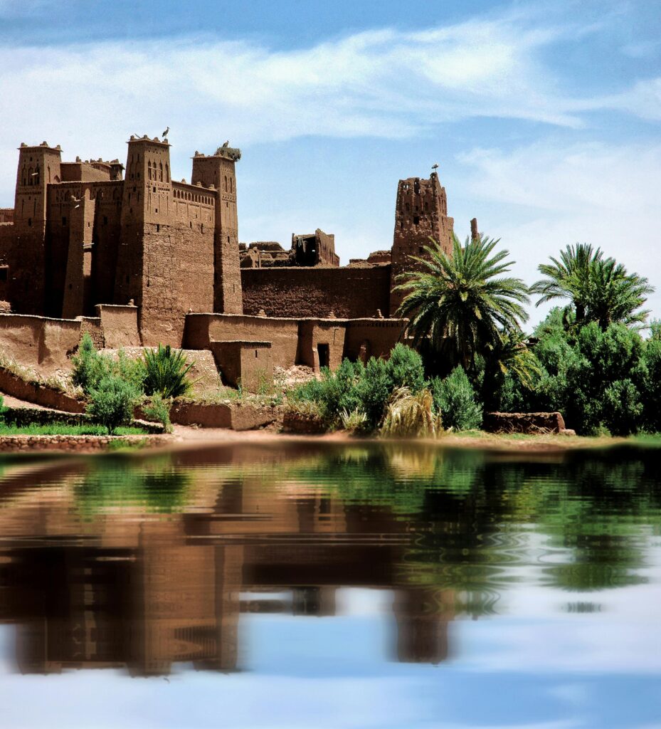 A scenic view of the ancient clay Kasbah Ait Benhaddou by the river in Morocco, under a clear blue sky.