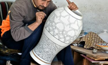 Artisan in Fès, Morocco intricately designs a large clay vase, showcasing traditional craftsmanship.