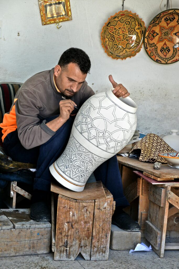 Artisan in Fès, Morocco intricately designs a large clay vase, showcasing traditional craftsmanship.