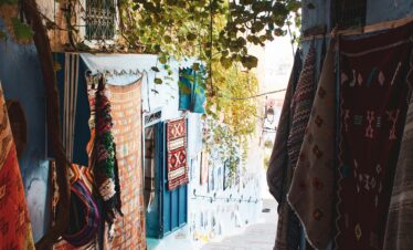 Picturesque narrow alley with vibrant rugs in the blue city of Chefchaouen, Morocco.