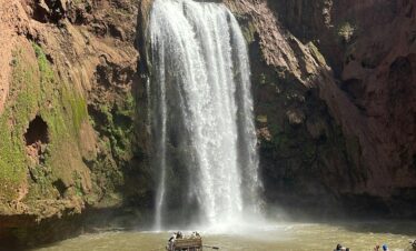 Capture of Ouzoud Waterfalls with tourists enjoying boat rides under the bright sun.