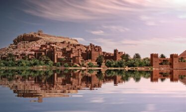 Picturesque reflection of Ouarzazate's historic ksar by the river under a vibrant sky.