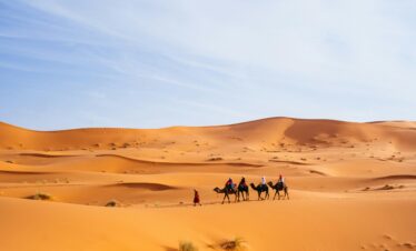 Tourists riding camels across the dunes of Merzouga, Morocco, a popular Sahara destination.