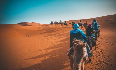 A group of people riding camels through the Sahara desert in Merzouga, Morocco at sunset.